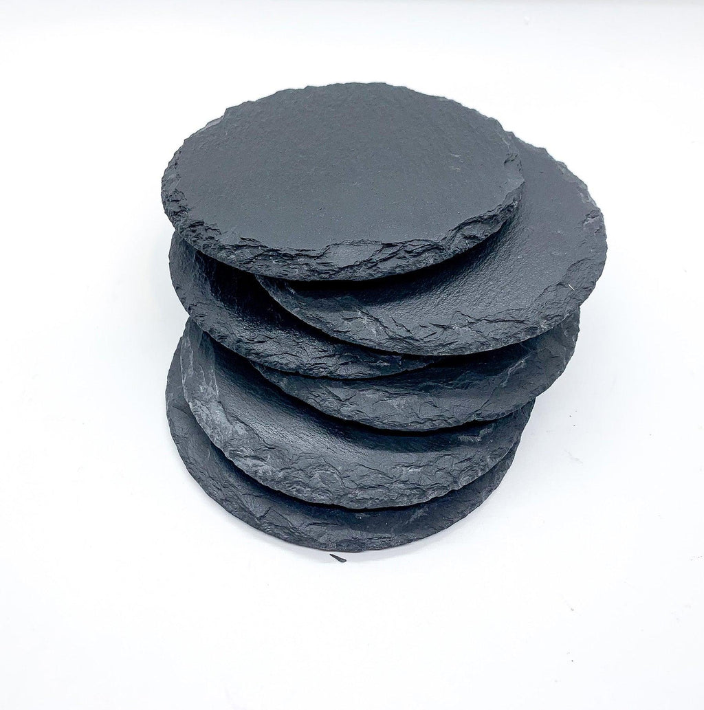 Stack of four dark gray natural slate coasters with rustic raw edges, photographed on a crisp white background to highlight the unique stone texture.