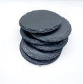Stack of four dark gray natural slate coasters with rustic raw edges, photographed on a crisp white background to highlight the unique stone texture.