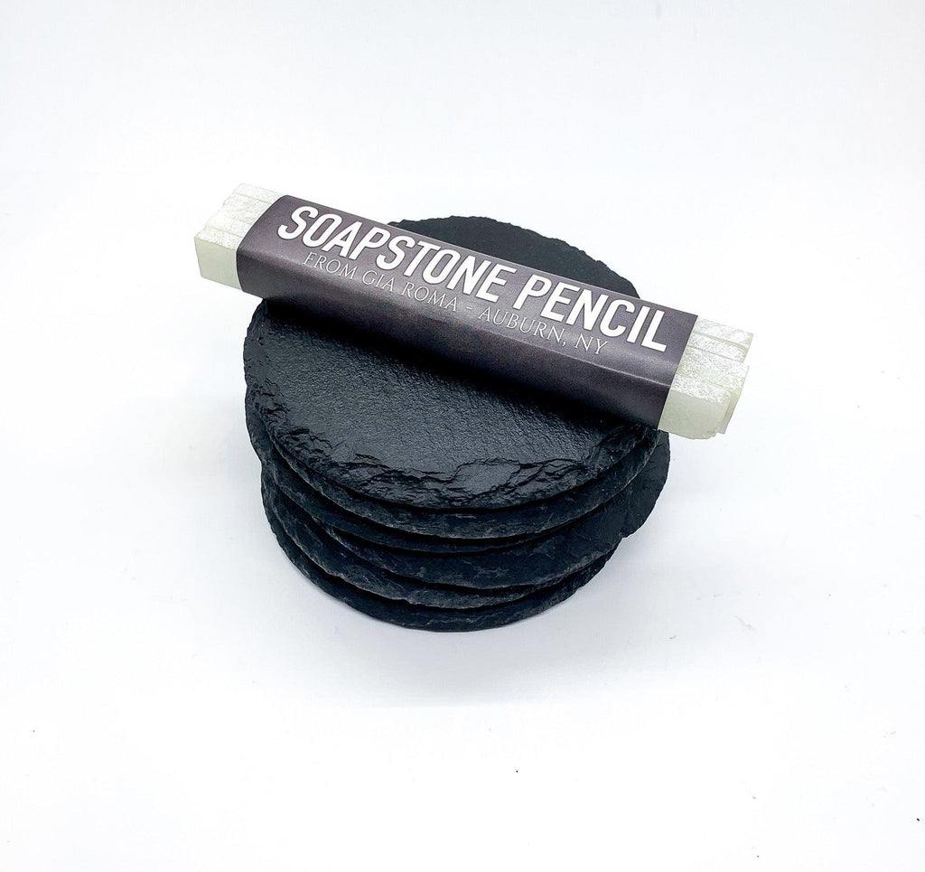 Handcrafted Gia Roma soapstone pencil resting on a stack of natural slate coasters to show how the stone can be easily labeled and customized.