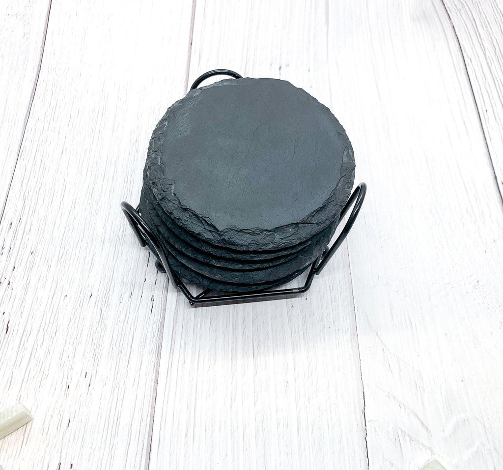 Stack of dark gray natural slate coasters stored in a matching black metal cradle holder on a light wood surface.