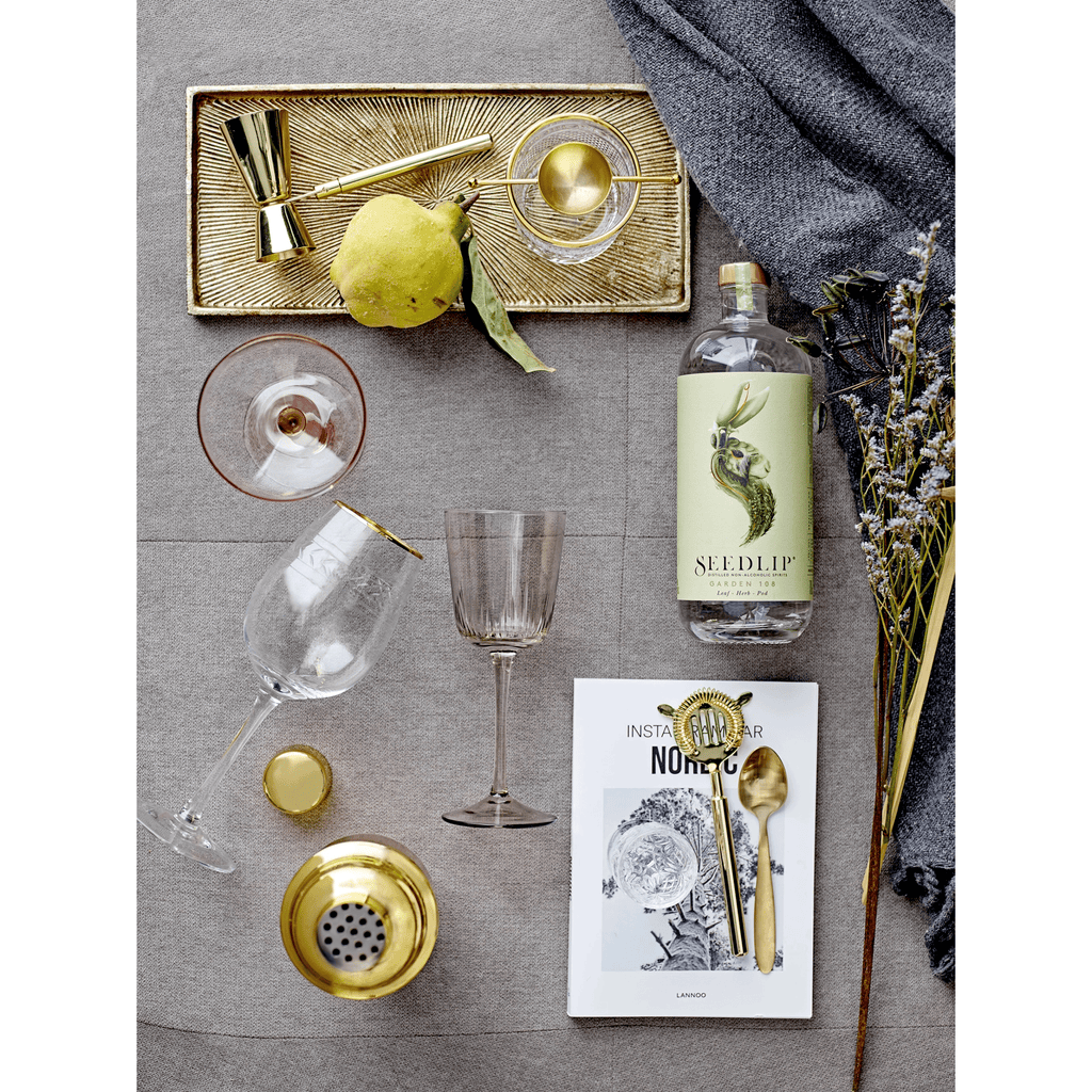 Elegant stainless steel cocktail shaker with a brass finish, styled on a dark rustic bar for the perfect home cocktail experience.