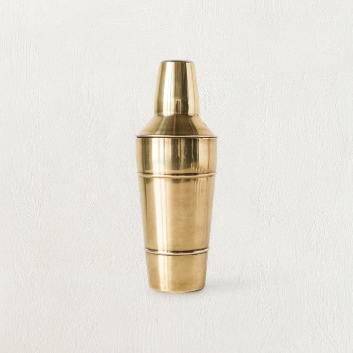 Stainless steel cocktail shaker with brass finish on a dark background.